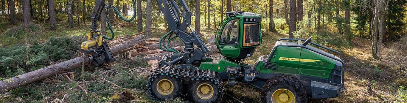 John Deere wheeled harvester in forest, harvesting trees with extended mechanical arm.