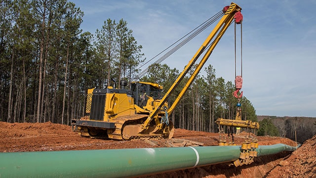 John Deere dozer equipped with sidebooms and winches laying pipe on a work site.