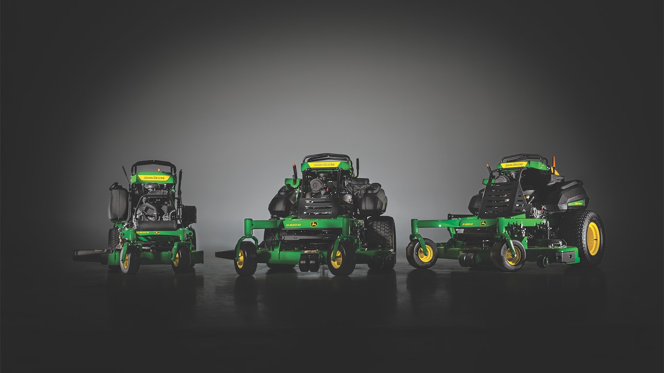 Indoor product group featuring one model each of the new E, M, and R John&nbsp;Deere QuikTrak 800 Series Stand-On Commercial Mowers in a silhouetted studio shot with a black background.