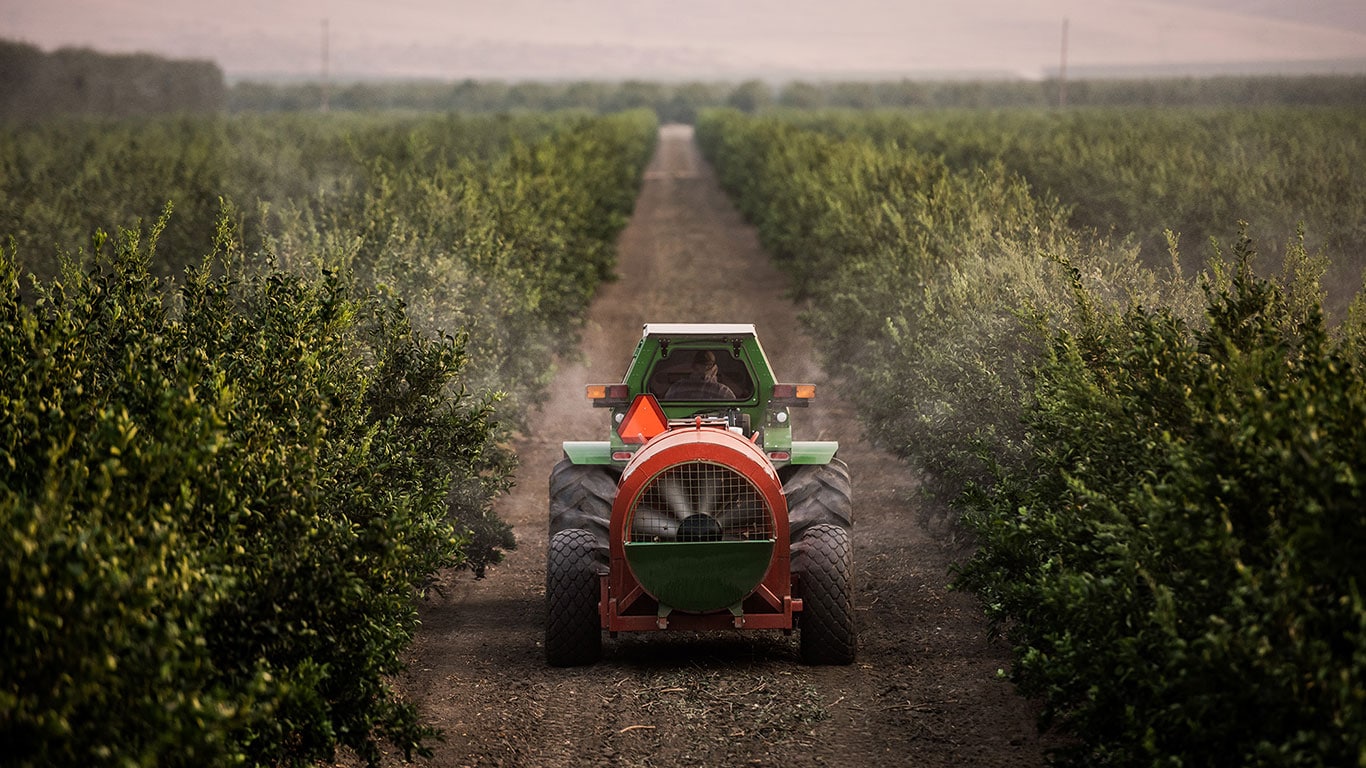 Smart Apply spraying chemicals to crops in a field during dusk.