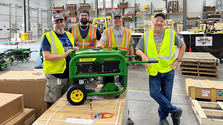 Four volunteers gather to show a John Deere engine powering a sump pump to help with flooding