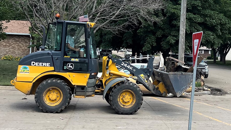 A volunteer drives a John Deere compact dozer through the streets of Rock Valley