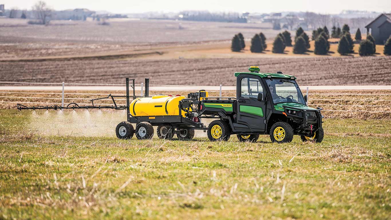 New John Deere Gator XUV 845R Signature Series Utility Vehicle with StarFire receiver in a field using a tank and sprayer boom rear attachment to apply chemical to the field on an overcast day