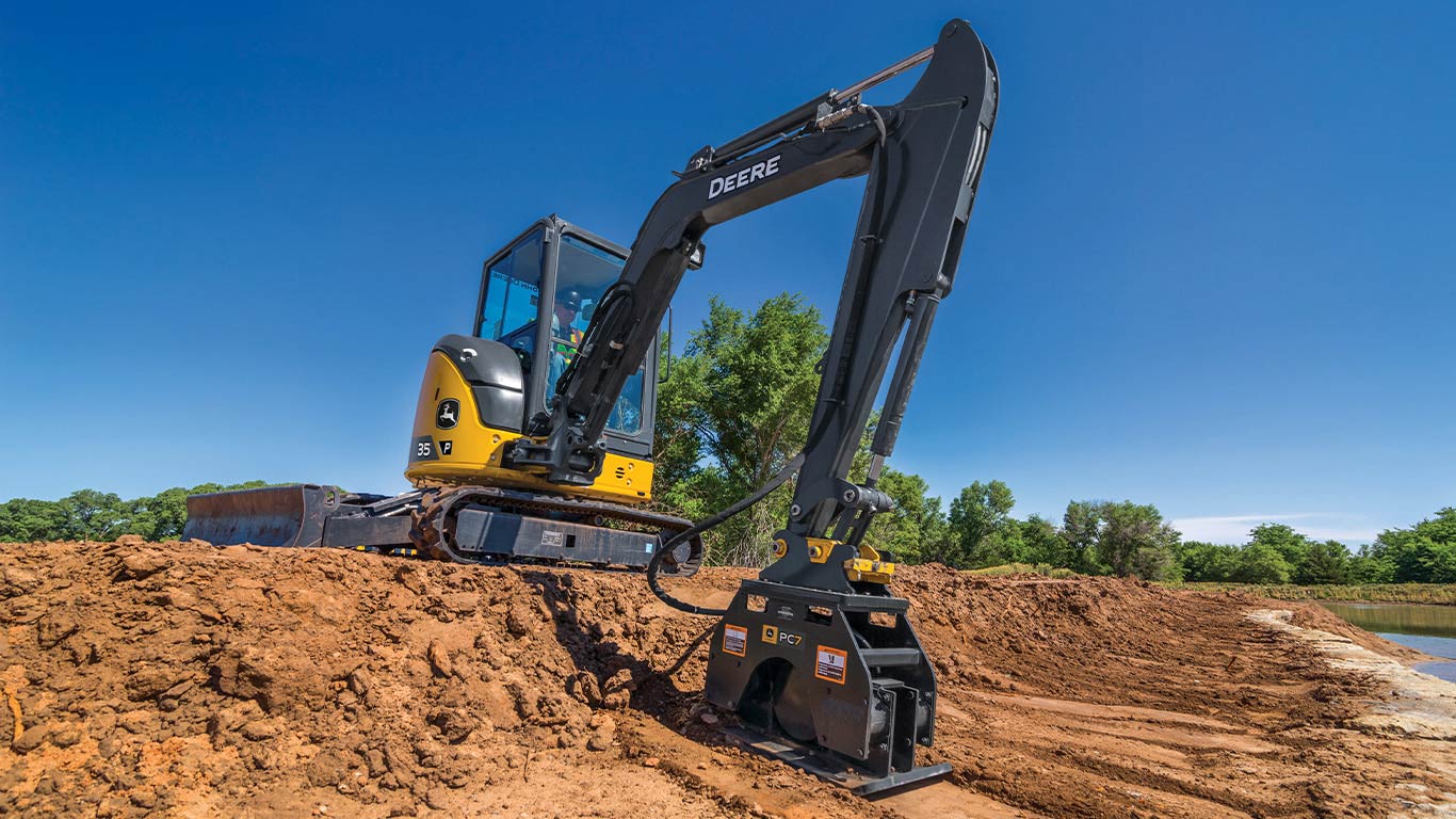 A John Deere 35 P-Tier Mini Excavator levels a dirt embankment at a construction site