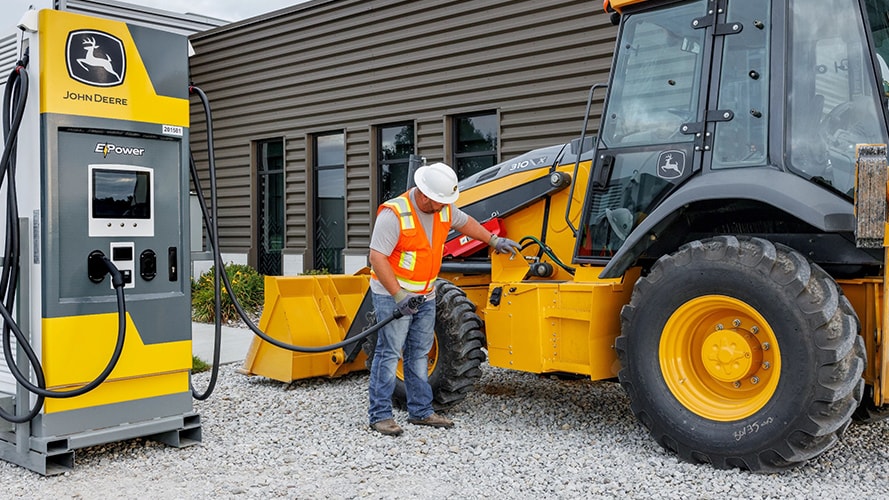 A construction worker plugging in a John Deere electric skid steer