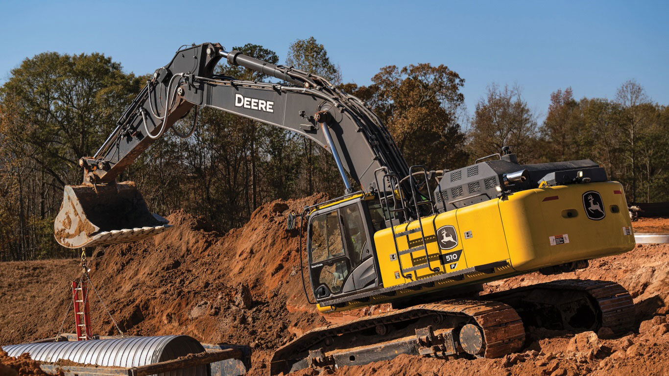 The 510 P-Tier Excavator lifting a pipe at a construction site with dirt mounds
