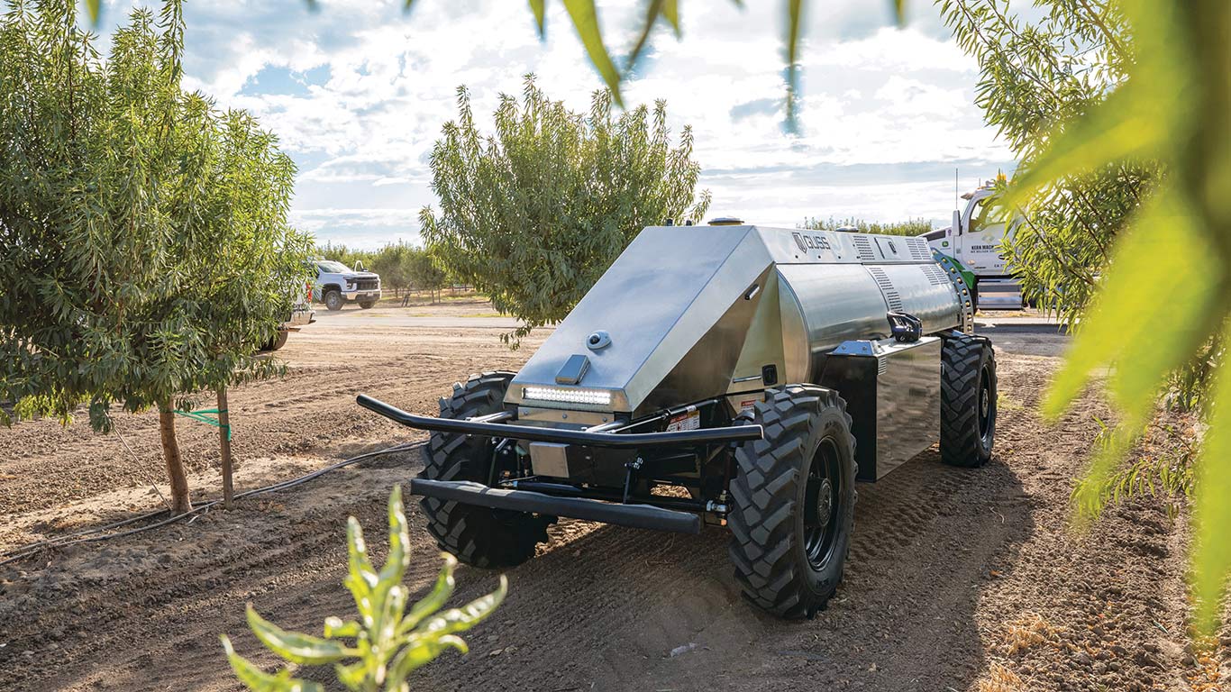Guss Automation sprayer front left angle in between plants with trucks behind it.