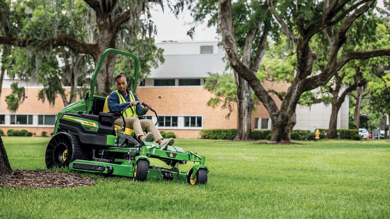 Operator on a John Deere Z997M ZTrak mowing near mulch bed around the base of a tree