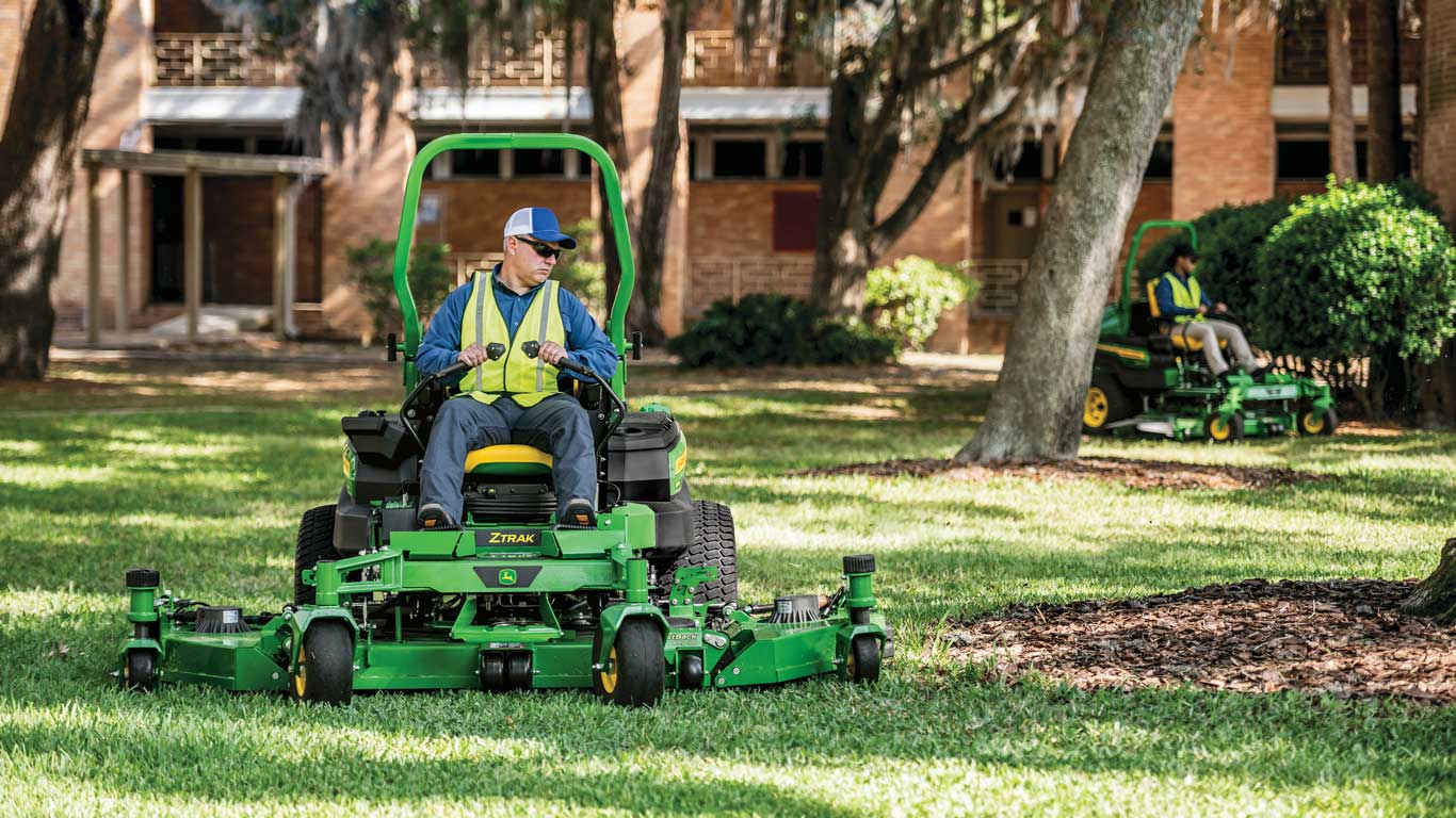In the foreground, an operator on a John Deere ZTrak mower, and in the background, another operator on a second John Deere ZTrak mower