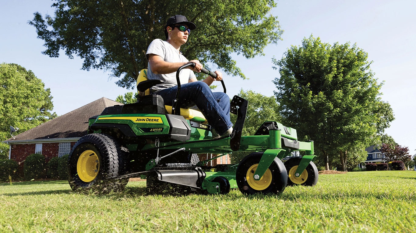 Customer wearing sunglasses is operating the new John Deere Z370RS Electric ZTrak Mower featuring EGO 56V ARC Lithium™ Batteries in a still action photo as grass exits the chute.
