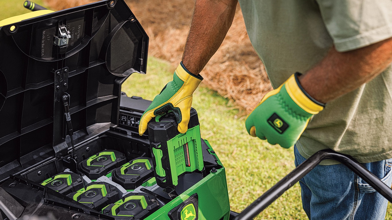 Operator viewed only from the chest down is shown wearing John Deere gloves as he holds one of six batteries from the new John Deere Z370RS Electric ZTrak Mower featuring EGO 56V ARC Lithium™ Batteries