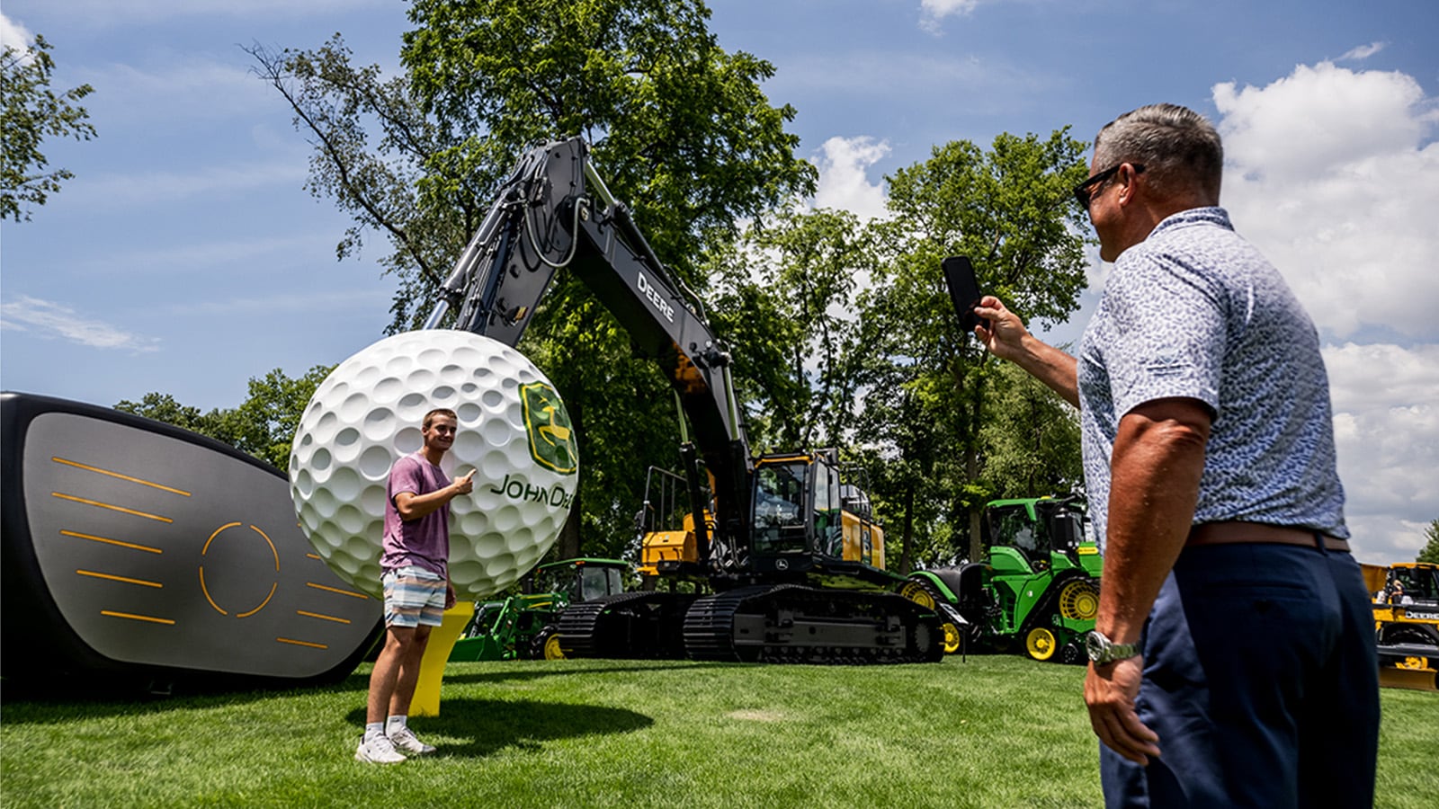 John Deere Classic spectators take a picture in front of a huge golf ball with excavator