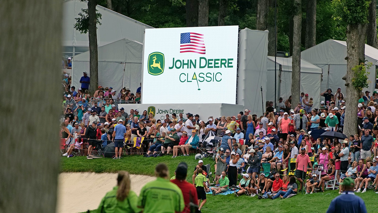 Professional golfers compete in the John Deere Classic with spectators watching from around the hole