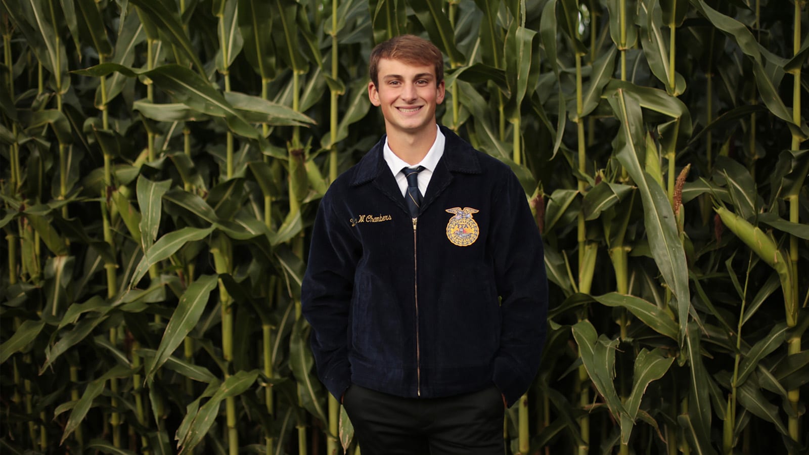 Zach Chambers stands in front of corn field in ffa jacket