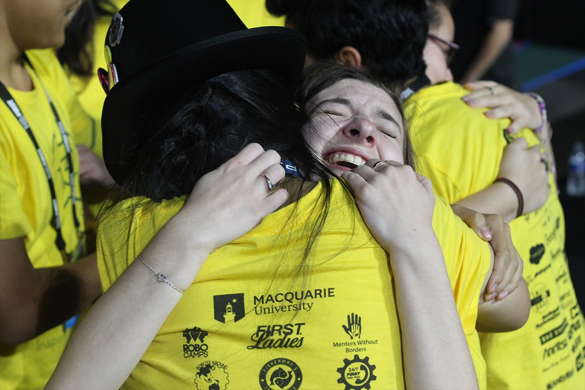 FIRST Robotics team members embrace while wearing competition shirts, capturing the impact of mentorship and women in STEM leadership.