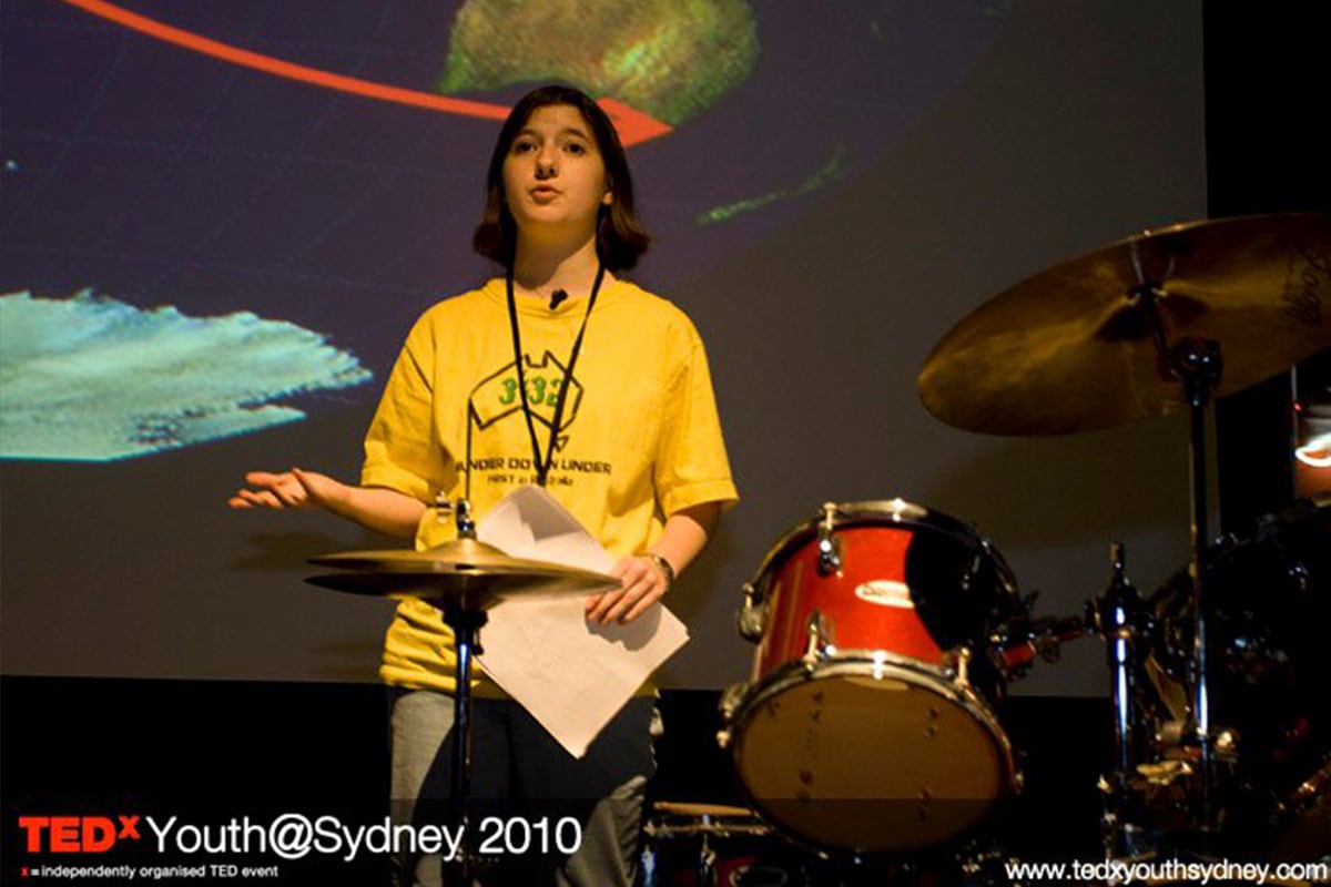 A speaker presents on stage at TEDxYouth Sydney, sharing lessons from FIRST Robotics and the power of STEM education.