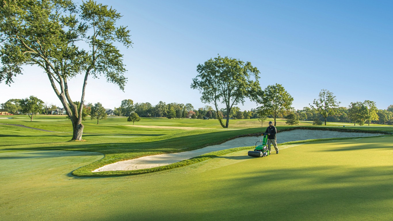 Person using a walk greens mower on a golf course