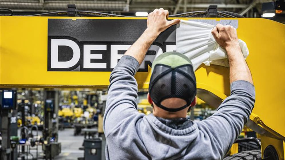 factory employee applies Deere decal on construction equipment