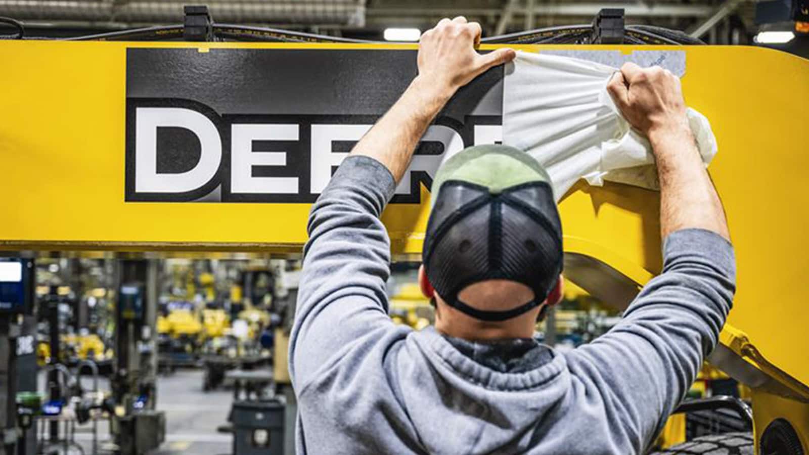 John Deere factory employee applies vinyl on equipment