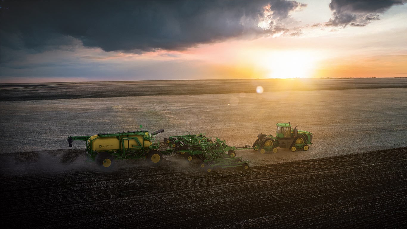 Tractor pulls an air cart across a wide field at sunset under dark clouds.