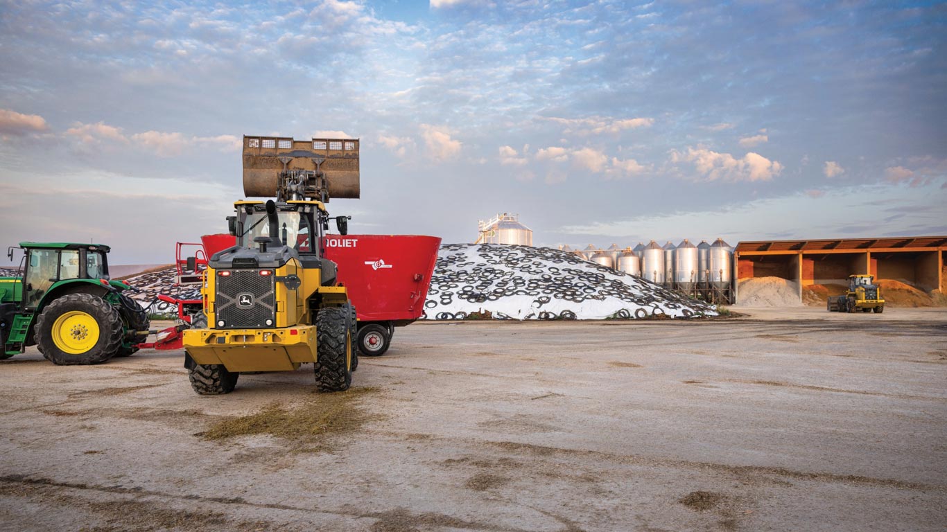 A John&nbsp;Deere 544 P-Tier loader with a raised arm, operating on a farm site.