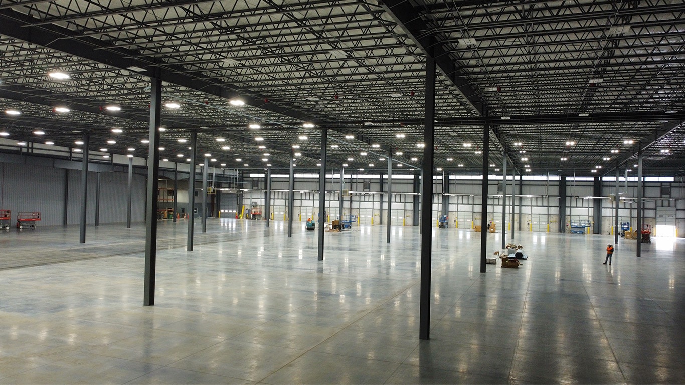 Wide interior view of the expanded John Deere Reman warehouse in Missouri, highlighting open floor space, structural columns, overhead lighting, and active construction equipment.
