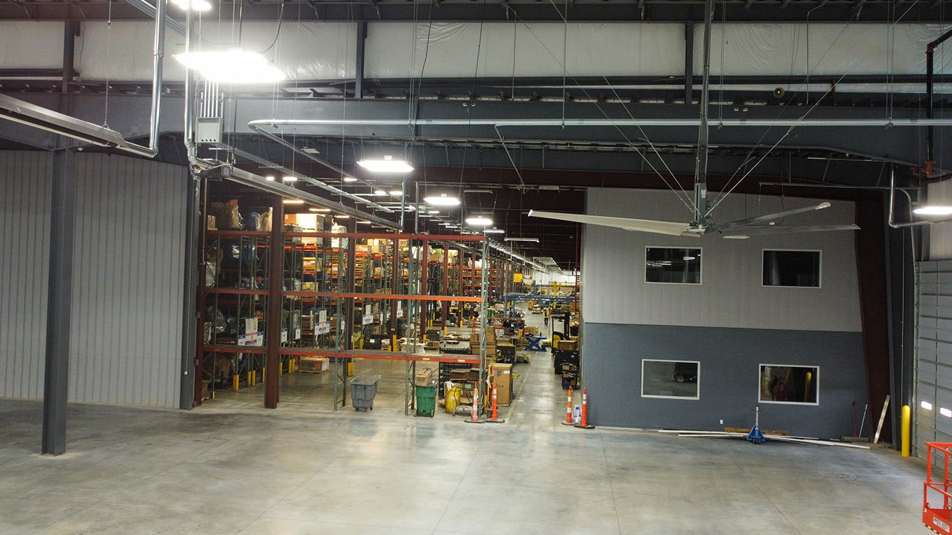 Interior view of the John Deere Reman facility expansion in Missouri, showing warehouse racking, work areas, lighting, and a newly built interior office structure.