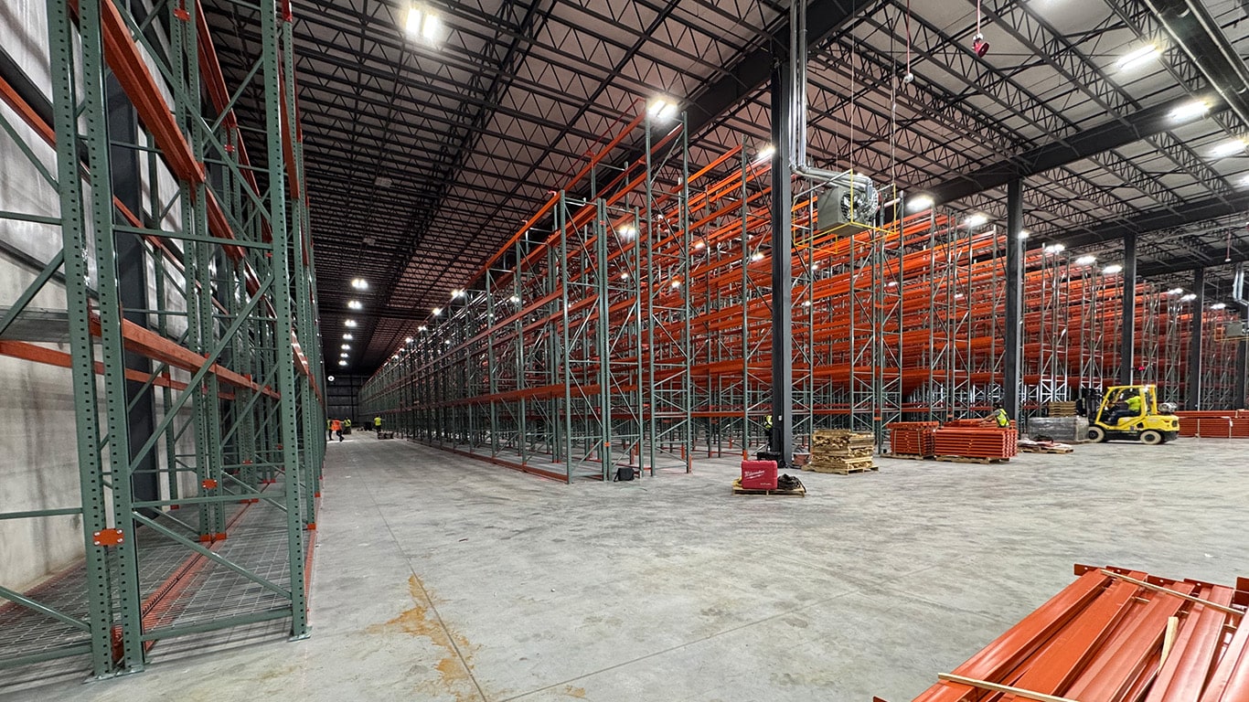 Interior view of the John Deere Reman facility expansion in Missouri, showing warehouse racking, work areas, lighting, and a newly built interior office structure.