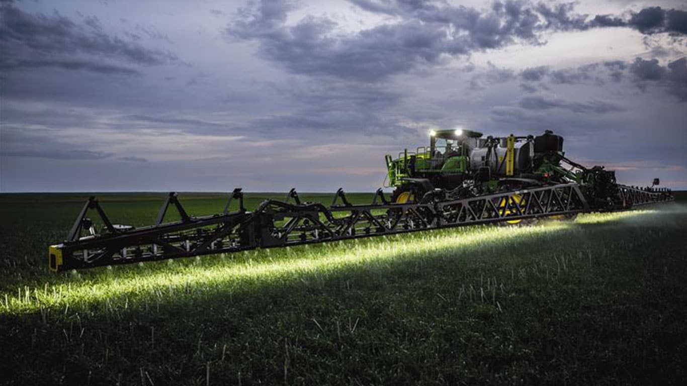 John&nbsp;Deere sprayer with bright lights running in field on a cloudy evening