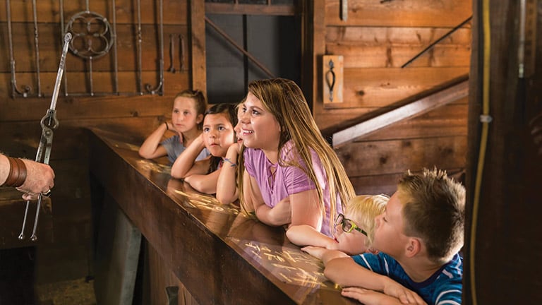 Children at the historic site admiring hand-crafted objects from the blacksmith