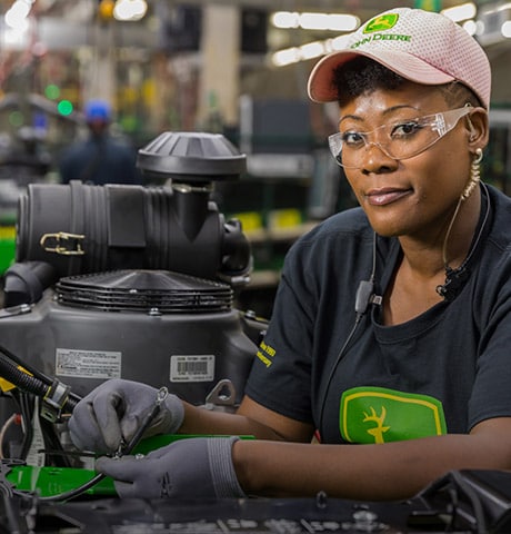 A smiling John Deere employee at a computer with a headset on.