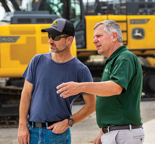 Dealer on the lot of the dealership showing a customer different models of excavators