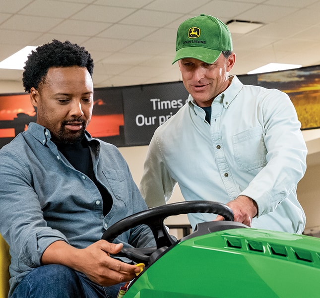 Customer sitting a riding lawn mower at dealership being assisted by a salesman