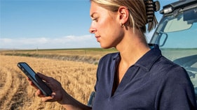 woman looking at phone near John&nbsp;Deere cab in wheat field