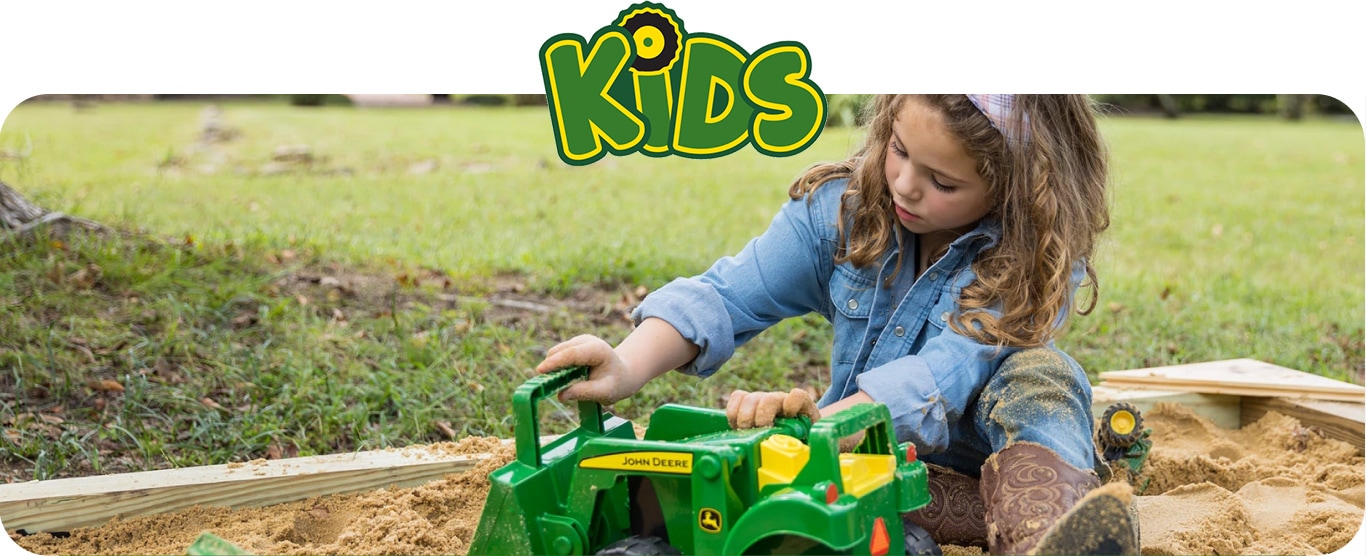 A young girl playing with a John Deere tractor toy in a sandbox