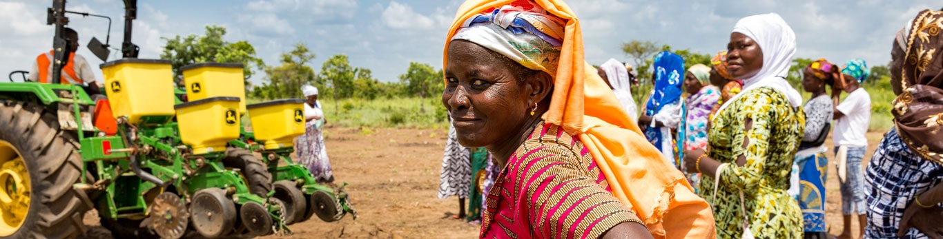 African woman in front of John Deere tractor and villagers.