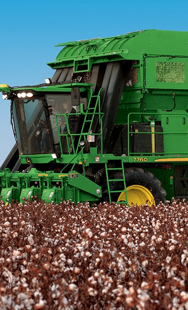 In a cotton field a John Deere cotton picker is harvesting and baling cotton