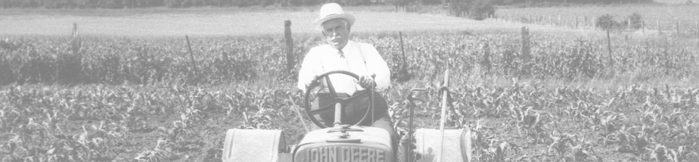 Toned black and white photograph of William Butterworth driving the tractor that is tilling a corn field on a green background