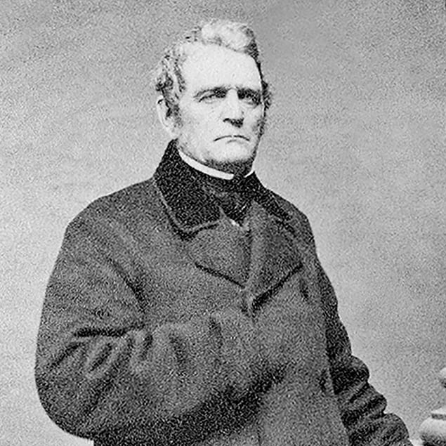 Black and white posed studio photograph of John Deere standing with his right hand in the flap of his winter coat	