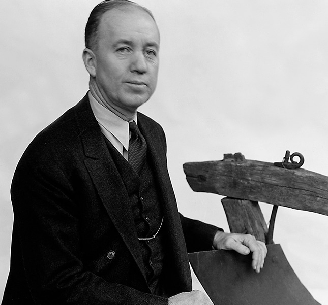 Black and white photograph of Charles Deere Wiman posed with an antique John Deere horse drawn plow	
