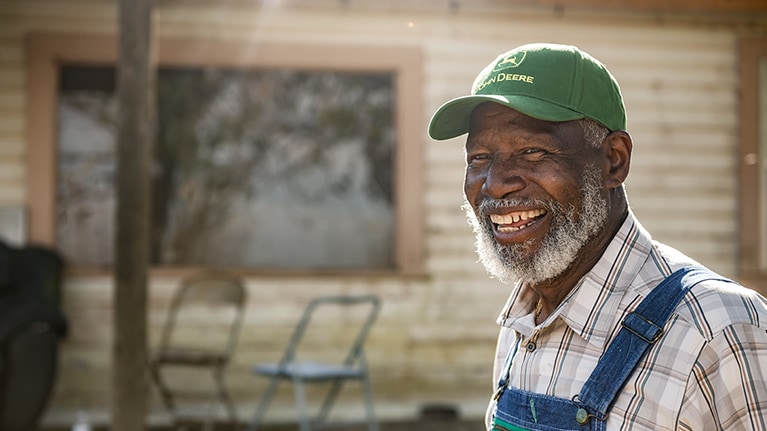 A smiling black farmer wearing a John Deere hat