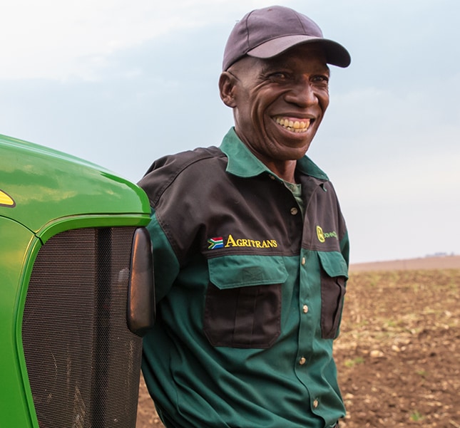 Proud male customer leaning against the front of his 5E Series Utility Tractor in South Africa