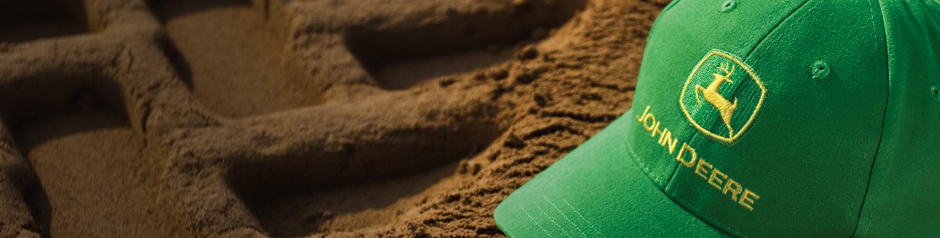 Green John Deere hat with the yellow and green logo set on top of dirt	