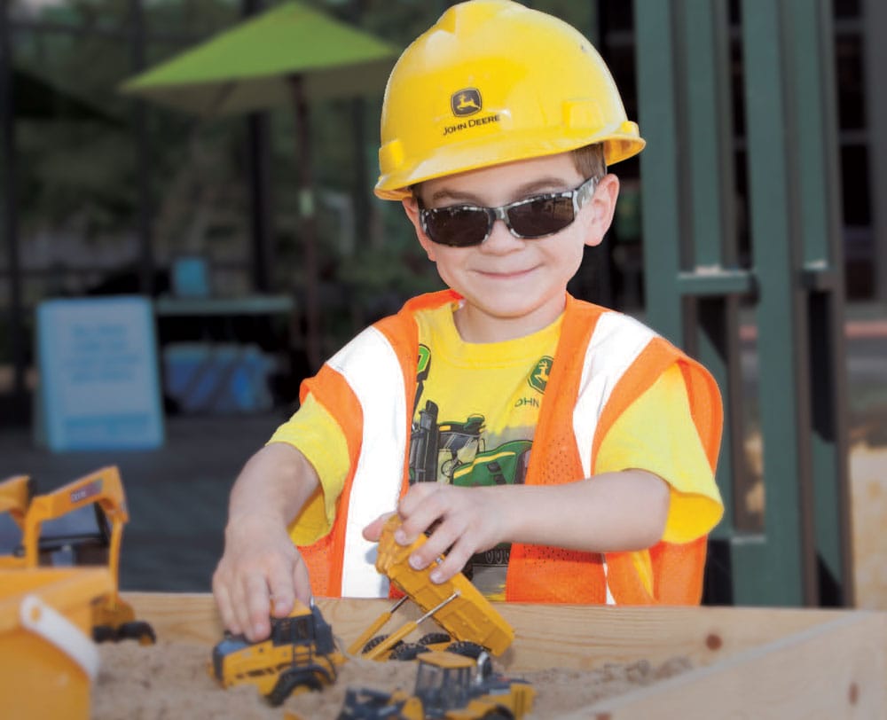 A child in a john deere helmet playing in a sandbox