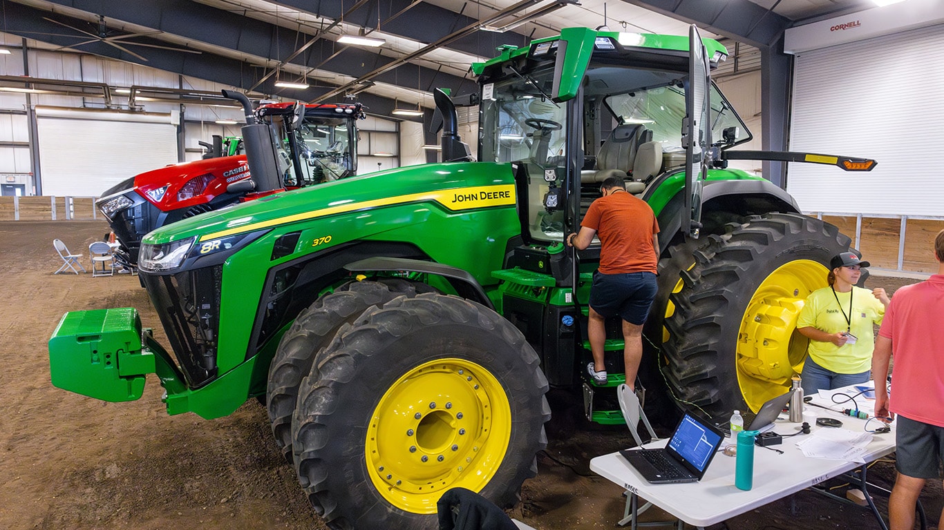 A student is climbing into a John Deere tractor at the CyberTractor Challenge.