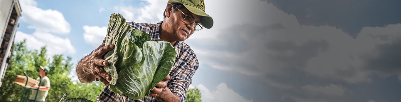 Un hombre con casco en un lugar de trabajo con equipos de John Deere cerca