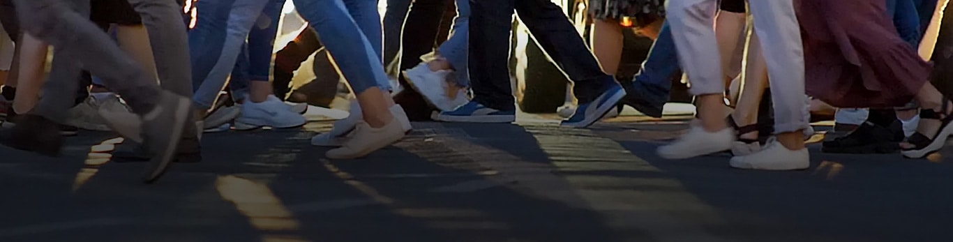 A city crosswalk showing dozens of people walking in opposite directions as they cross the street