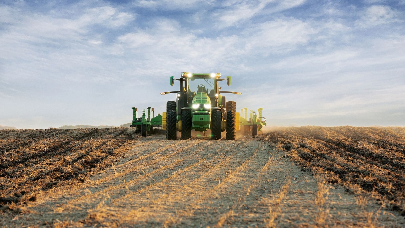 Tractor John Deere autoconducido que tira del equipo de laboreo a través de un campo abierto.