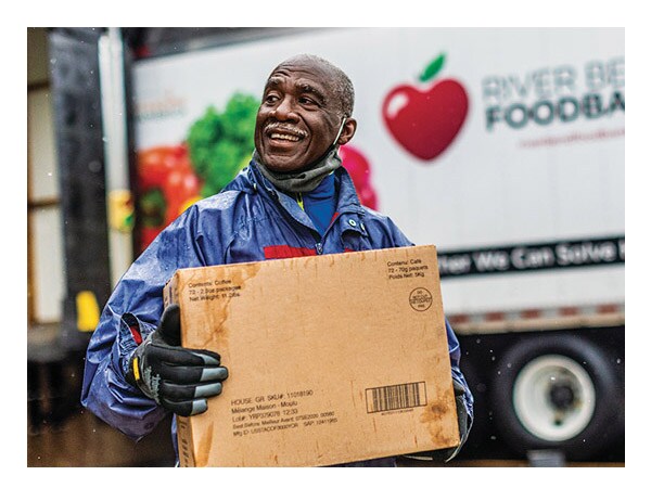 A smiling man carrying a box from a River Bend Food Bank truck