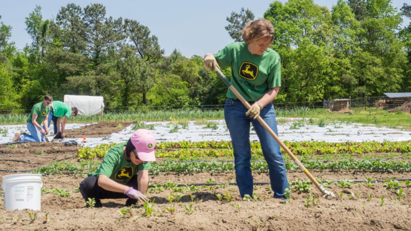 two women planting and weeding in a large garden with trees and